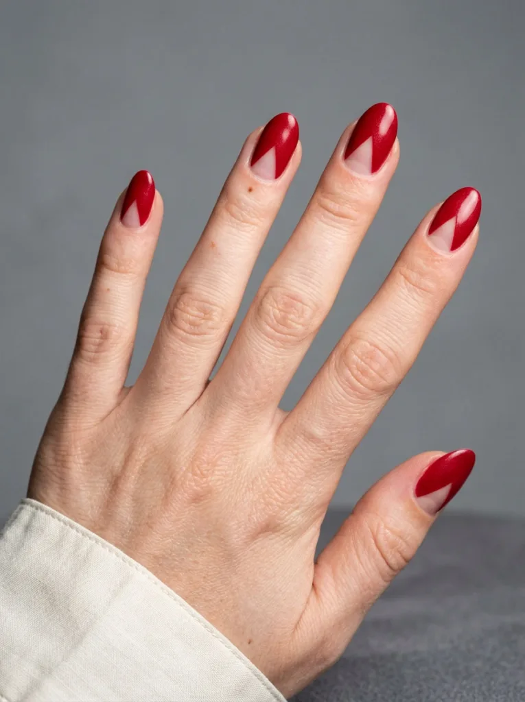 Hand with red negative space nail art fanned against a plain gray studio backdrop.