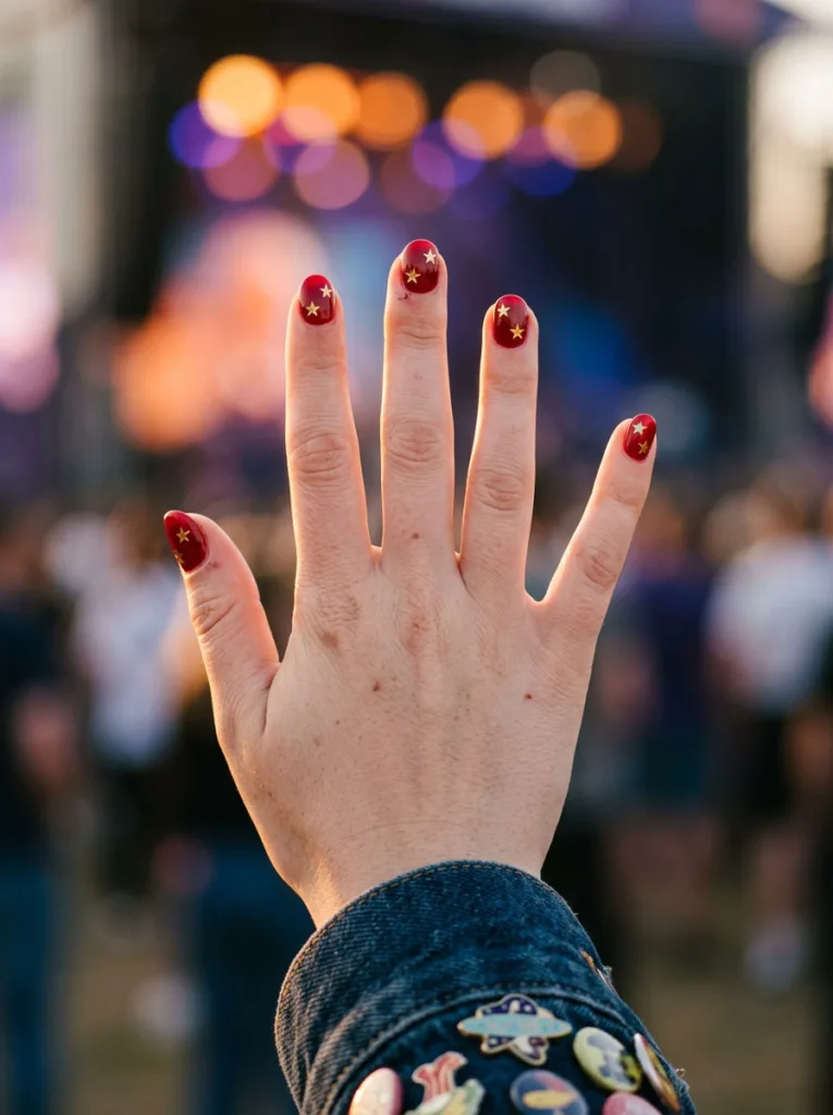 Hand with red star nail art held up against a festival crowd at dusk.
