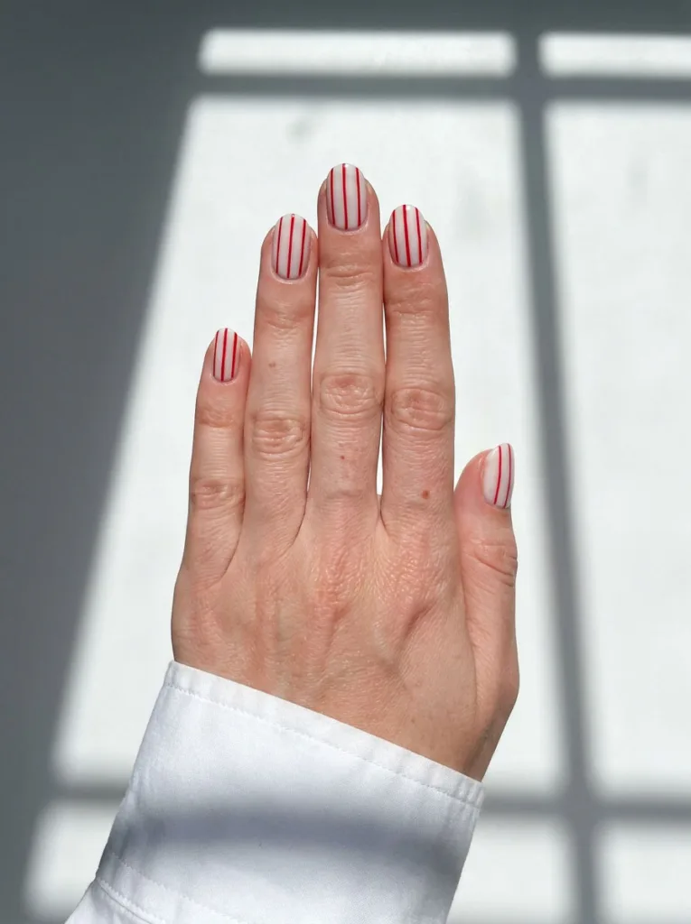 Hand with red striped nail art against a graphic shadow pattern on a white surface.