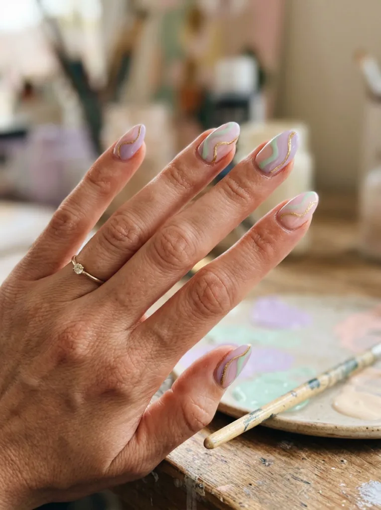 Abstract pastel swirl easter nails with gold line accent near paint palette