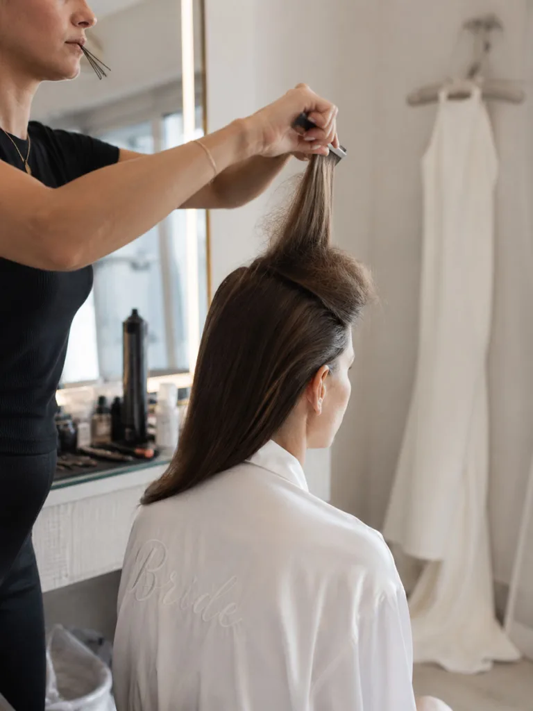 Hairstylist backcombing the base of a bridal ponytail for all-day hold before the wedding