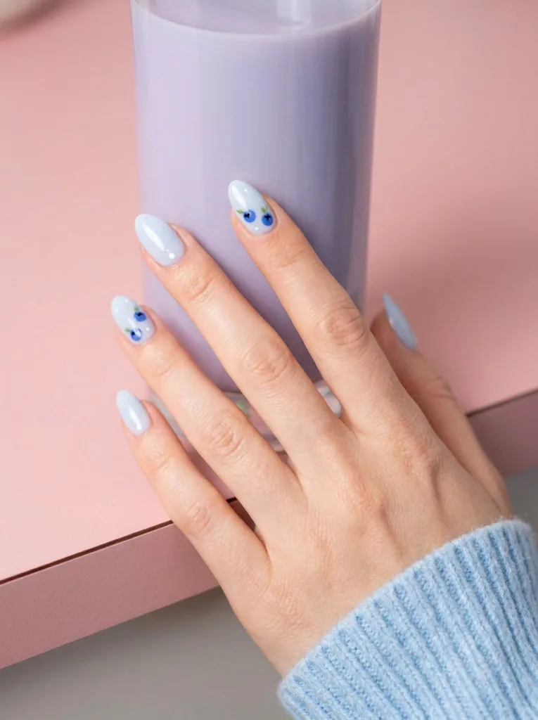Blueberry milk fruit nail design on a hand beside a glass of blueberry milk