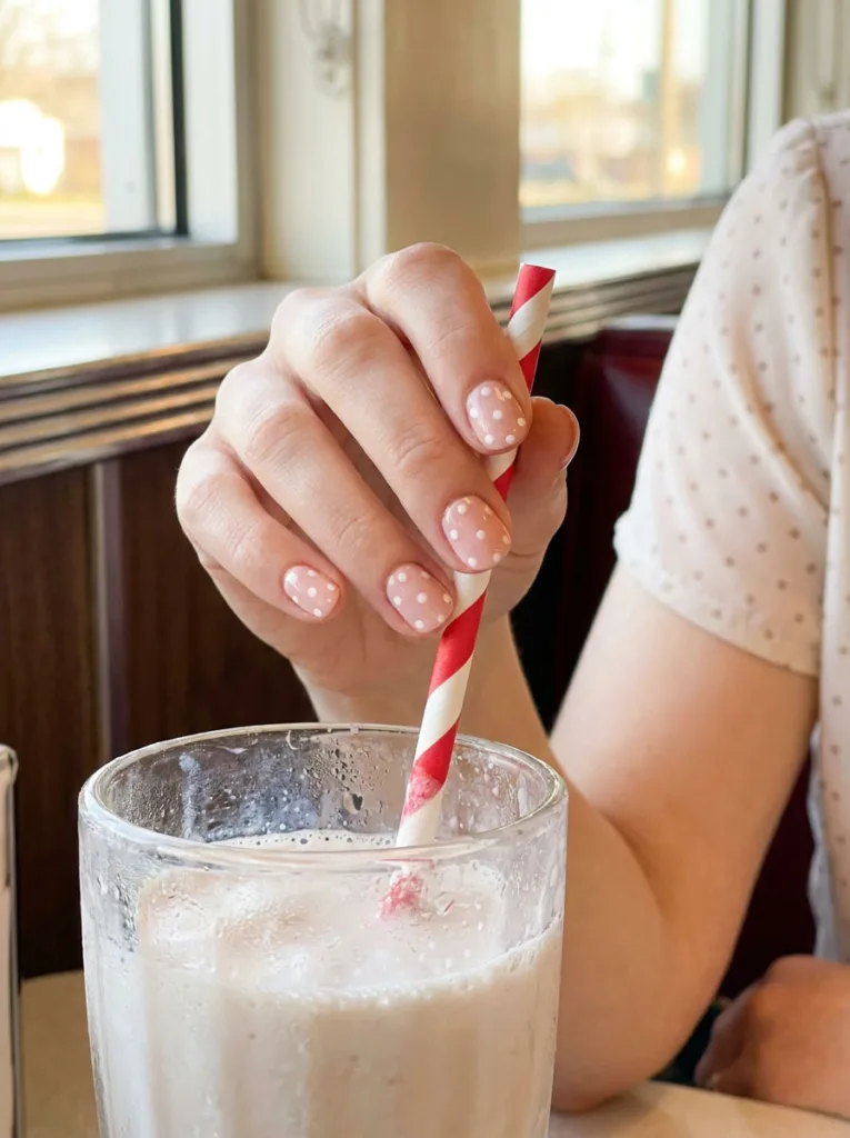 Blush pink polka dot nail art on squoval nails wrapped around a milkshake straw