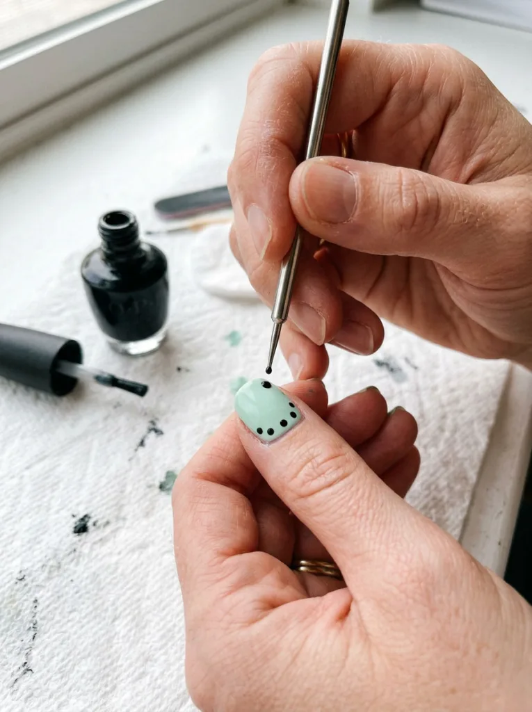 Hand using dotting tool to create speckled egg easter nail design