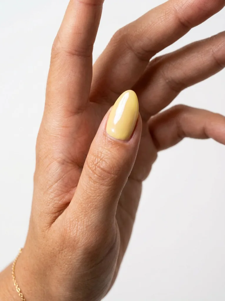 Fair-skinned hand with glossy glazed butter yellow nails against a white studio backdrop