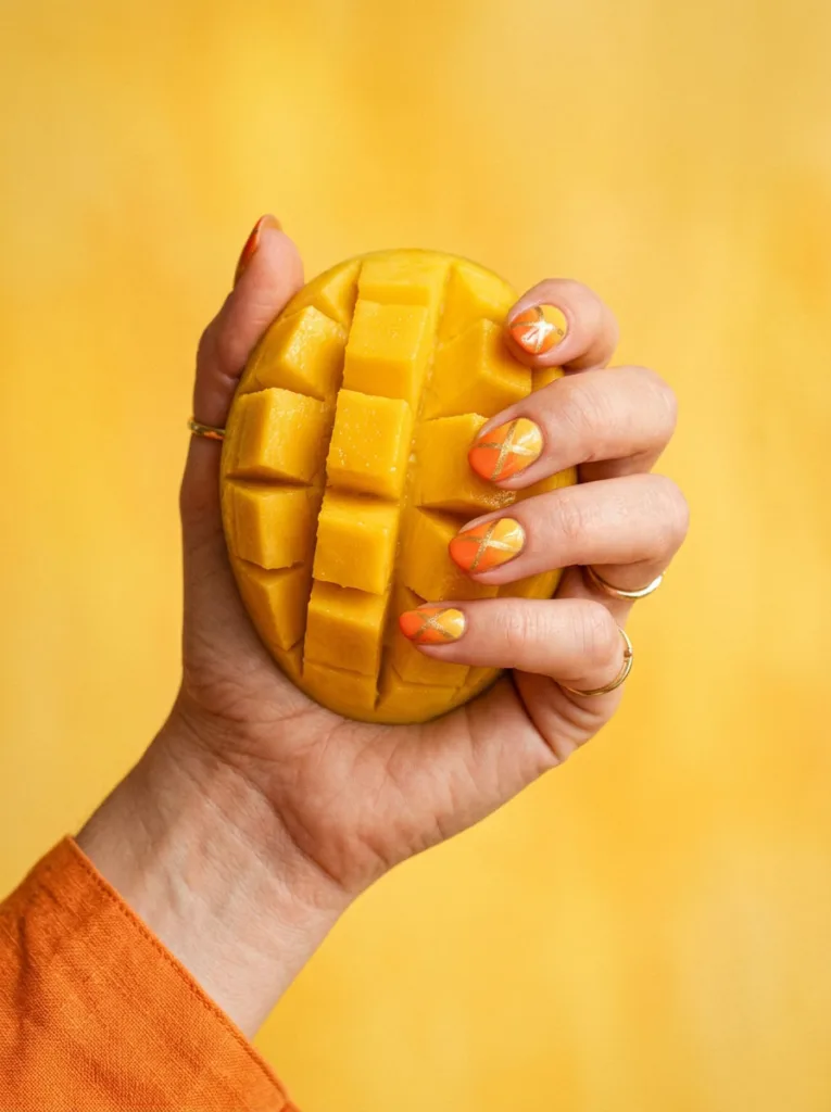 Mango cheek fruit nail design on a hand holding a diced mango half