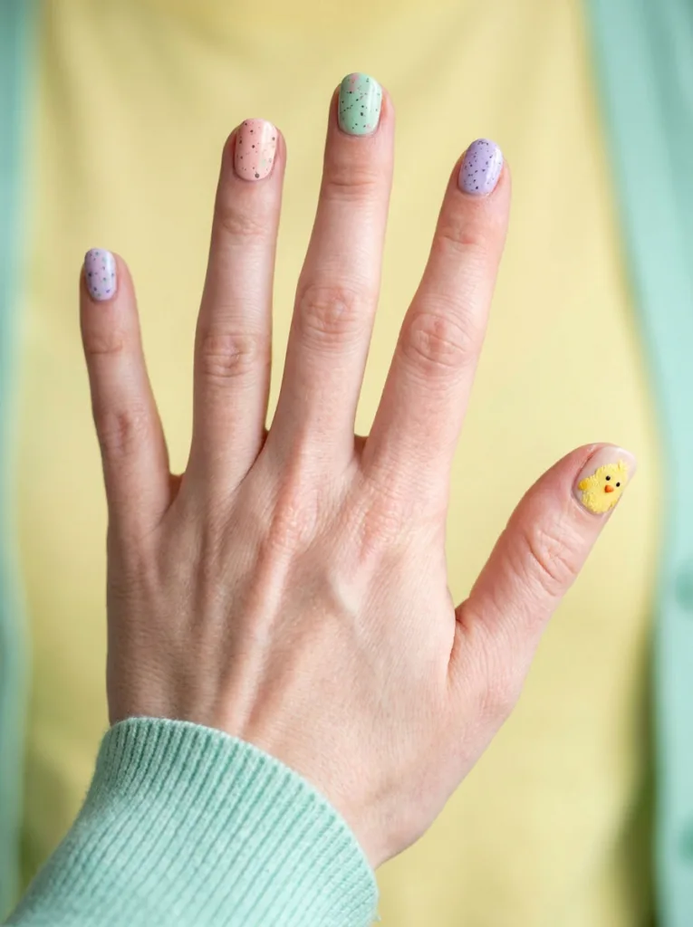 Mismatched chick and speckled egg easter nail design on spread fingers