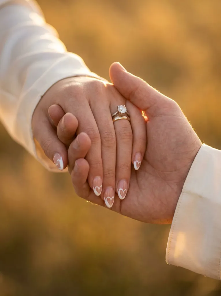 Negative space heart wedding nail design on hands clasped with a partner's hand
