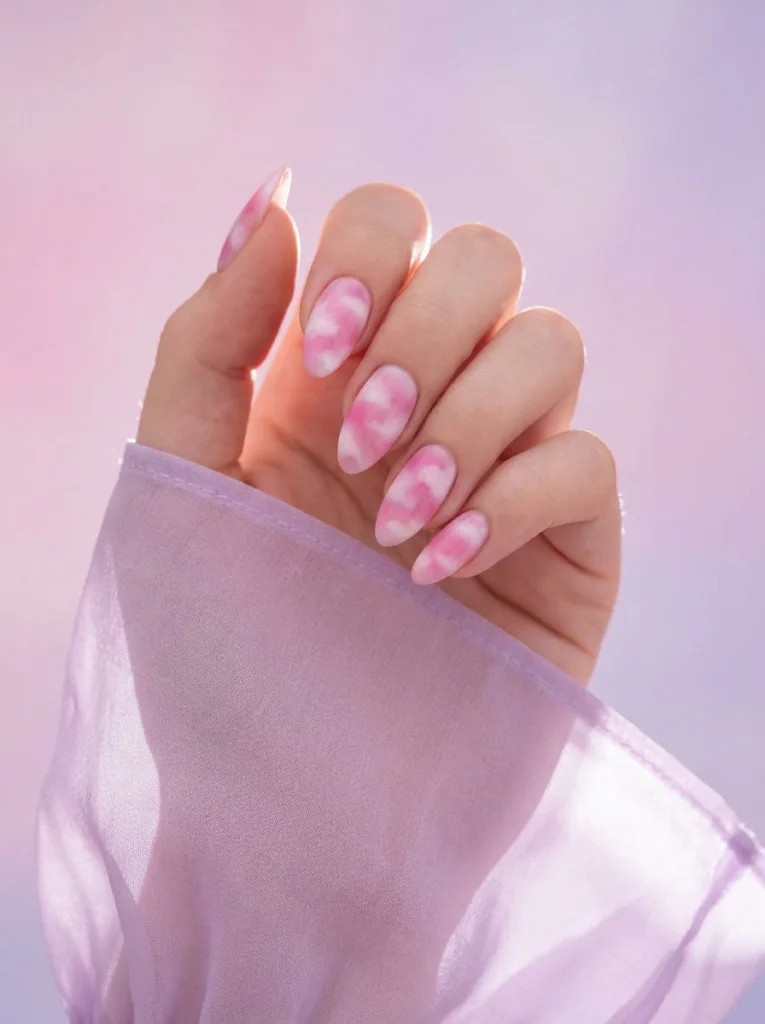 Airbrushed pink and white aura nail art on almond nails raised toward the light