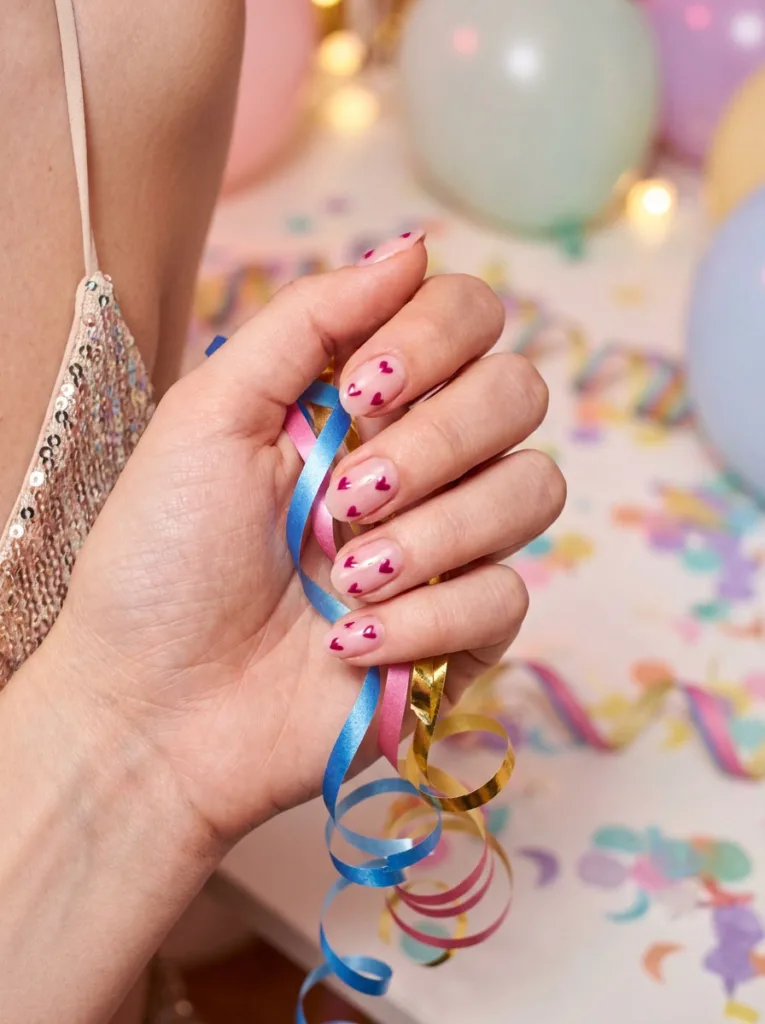 Sheer pink nail polish with tiny hand-painted hearts holding a balloon ribbon