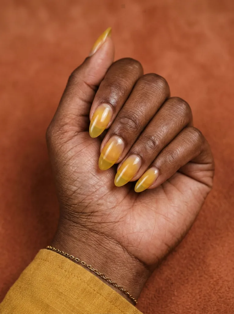 Deep skin tone hand with sheer yellow jelly nails against a warm terracotta backdrop