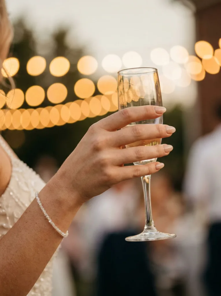 Short almond nude wedding nails holding a champagne flute at a reception