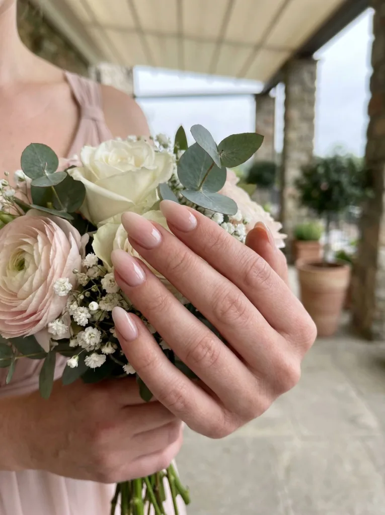 Soft ombre blush wedding nails holding a bridal bouquet outdoors