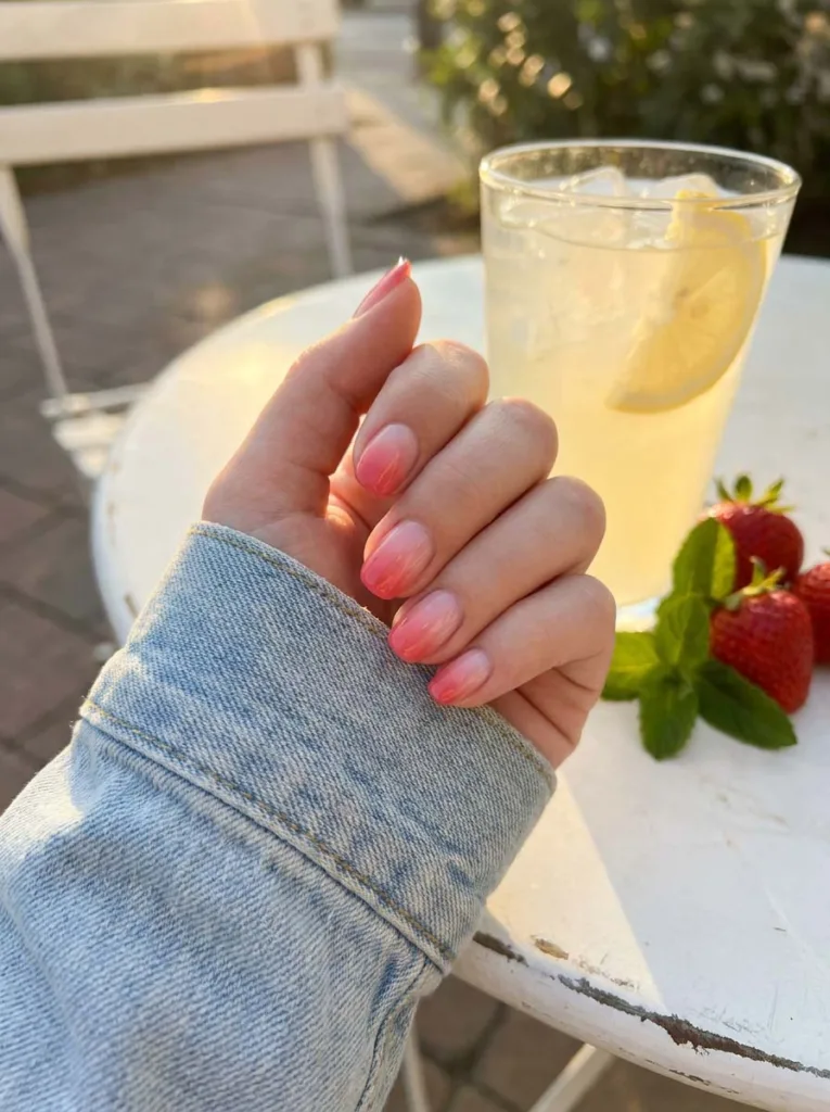 Strawberry milk ombre nail gradient with fresh strawberries on an outdoor café table