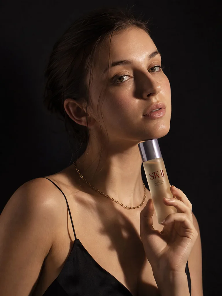 Woman in an elegant black dress holding a luxury fermented Korean essence bottle in dramatic studio lighting