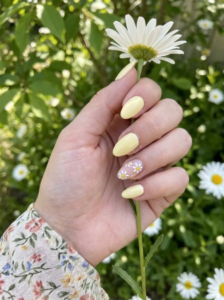 Fair-skinned hand with yellow daisy nail art holding a real daisy flower in a garden