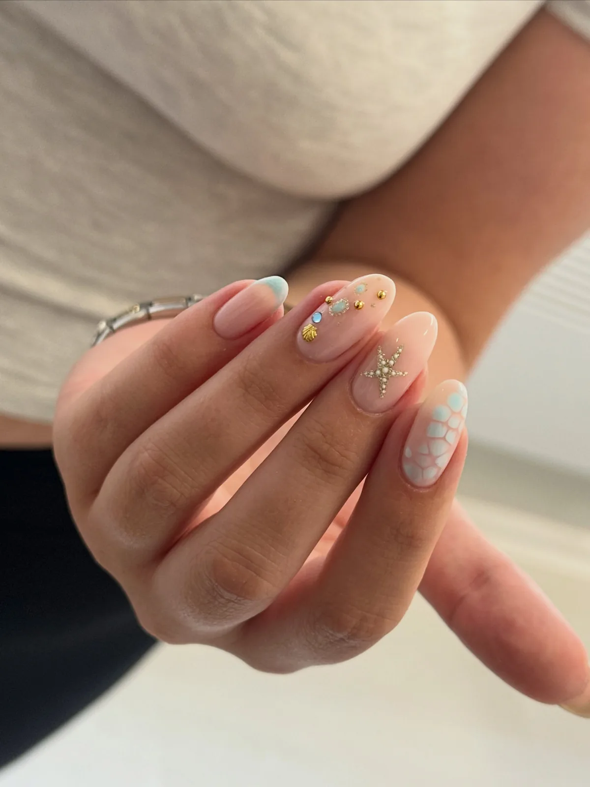 Sheer pink ocean nails with blue details, gems, a starfish and a gold shell charm