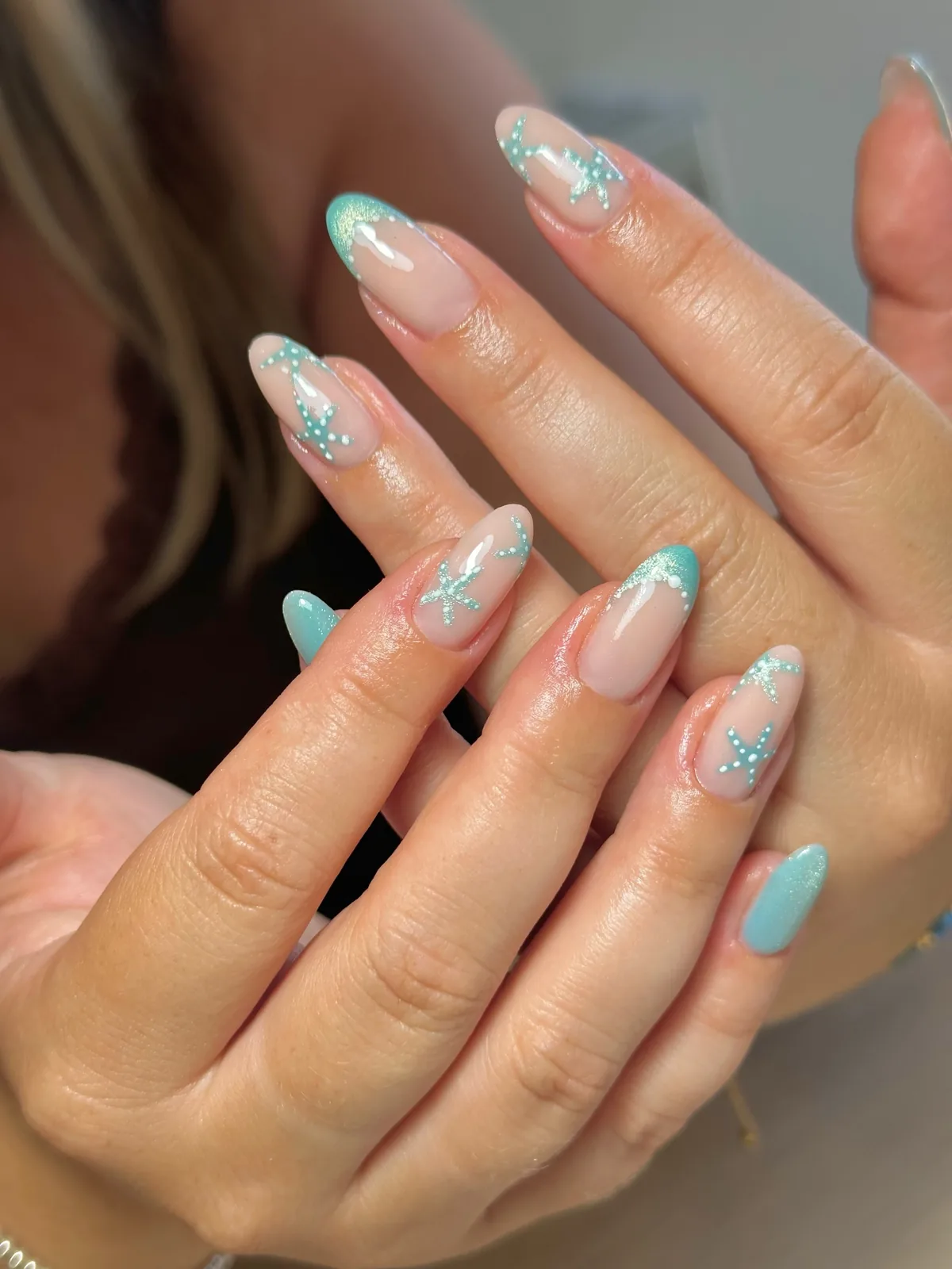 Glossy pink nails with teal French tips and dotted teal starfish