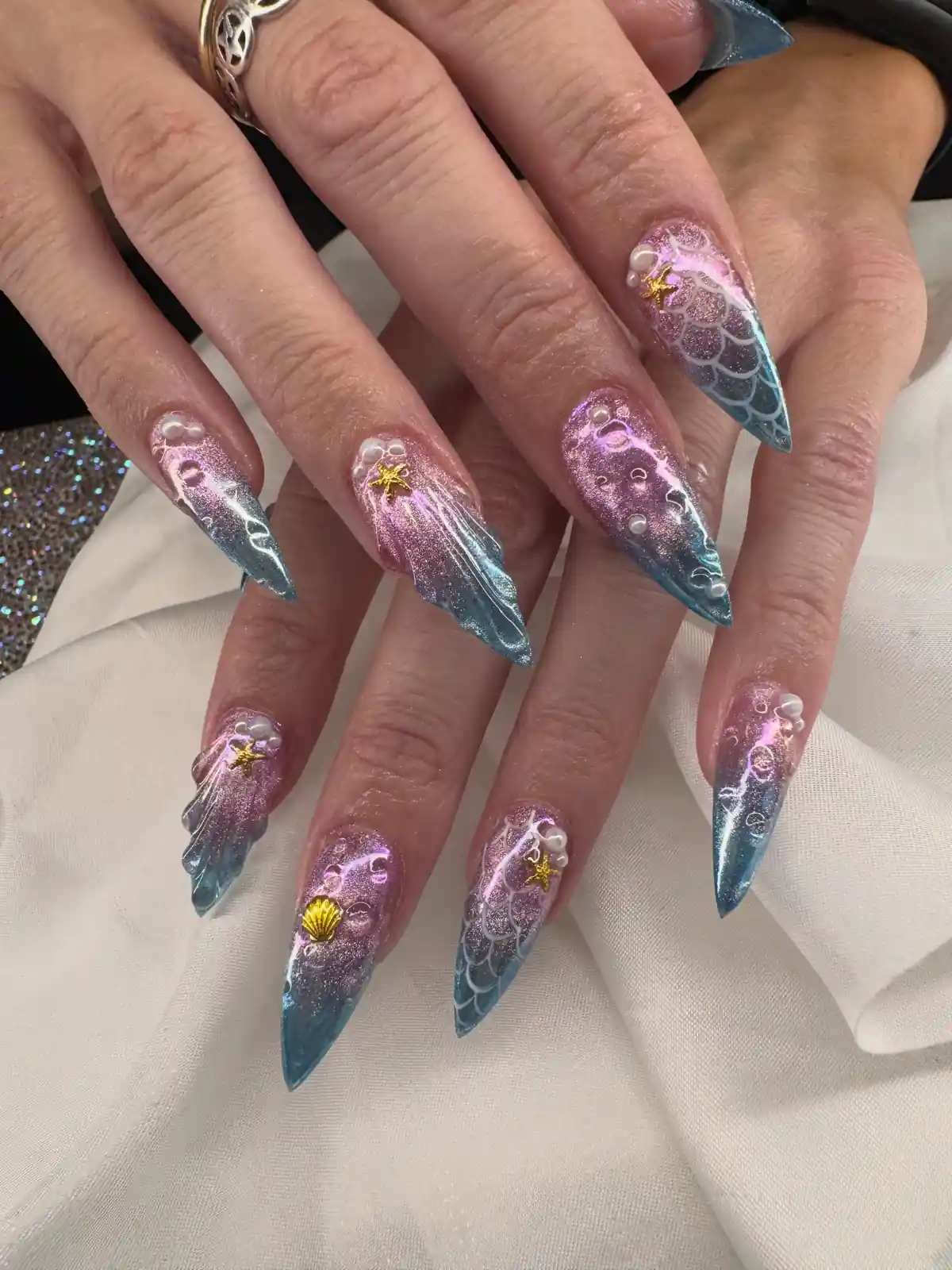 Long pink and teal nails with scale outlines, raised bubbles and gold ocean charms