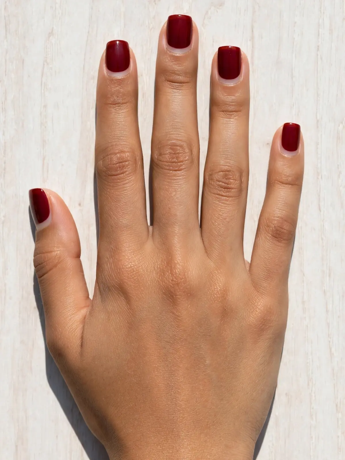 Negative space half-moon design with bare base and oxblood polish on short square nails, dorsal hand on white oak