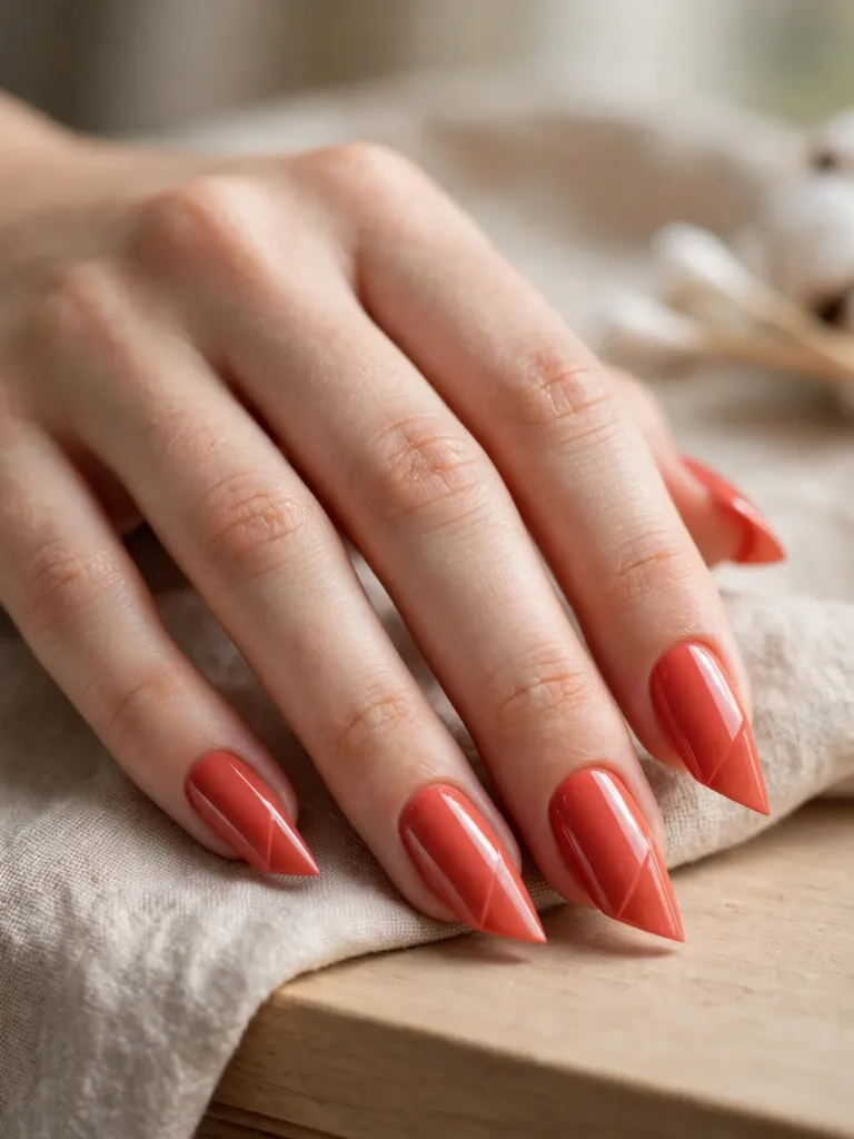 Close-up of lipstick-shaped nails in coral polish with a sharp diagonal slanted tip